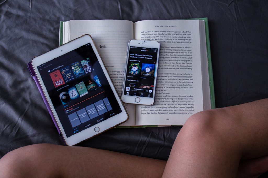 open book, ipad, and iphone on bed