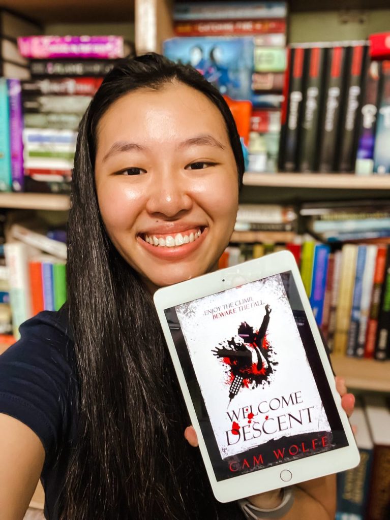Charmaine holding an ebook copy of Welcome Descent next to her face while she smiles
